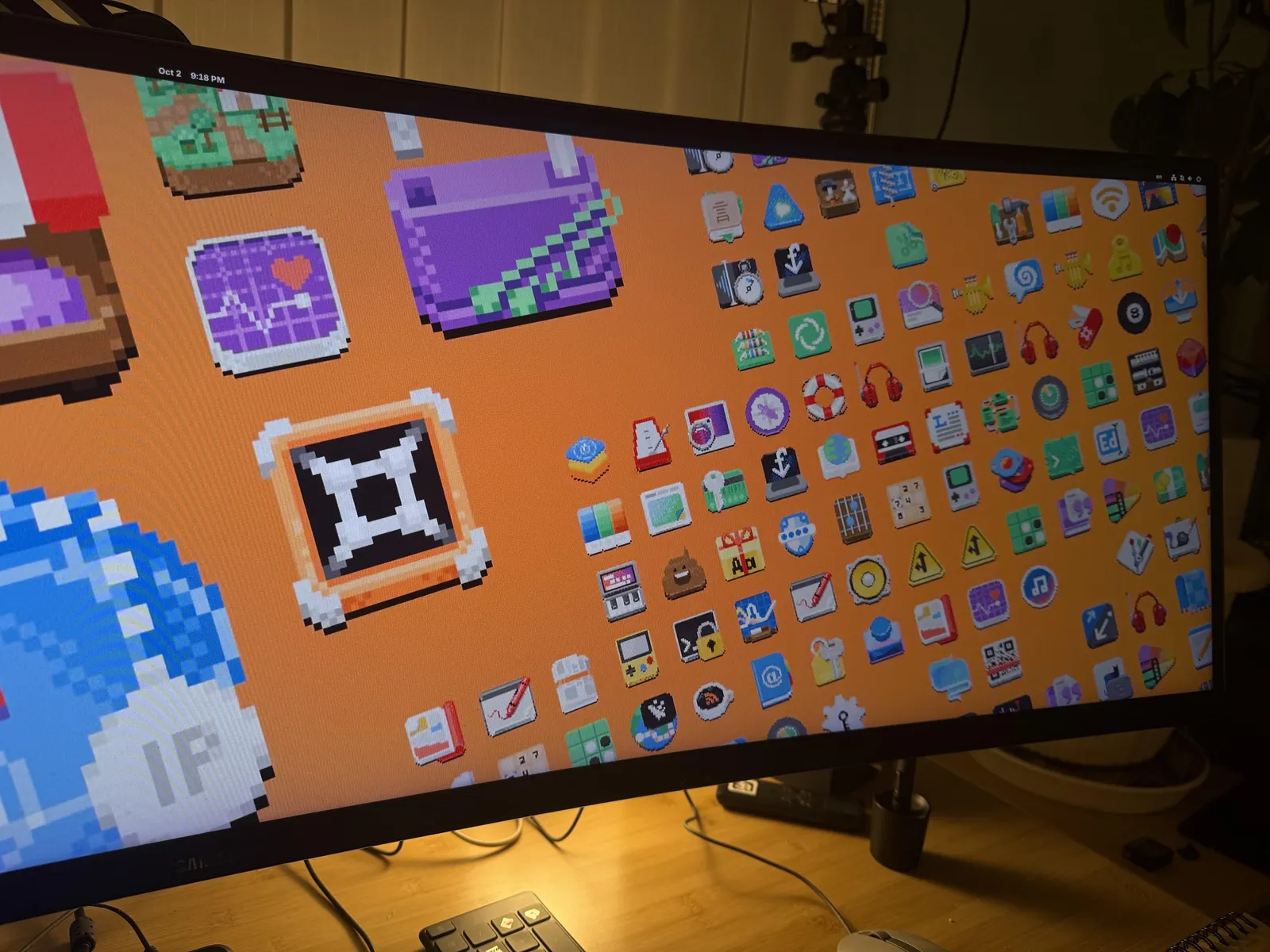 Orange pixel art wallpaper variant with large foreground icons, photographed on a monitor